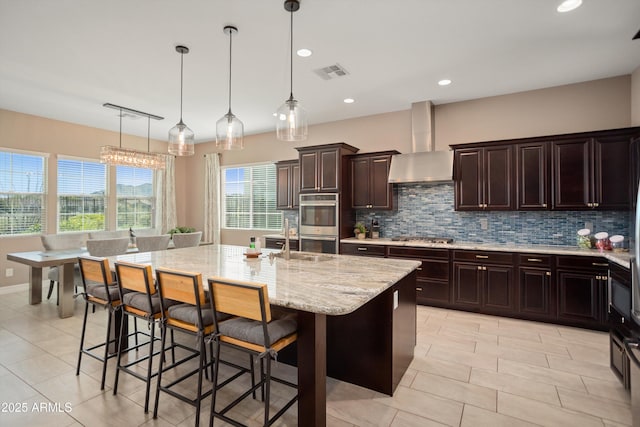 kitchen featuring wall chimney exhaust hood, a breakfast bar, visible vents, backsplash, and appliances with stainless steel finishes