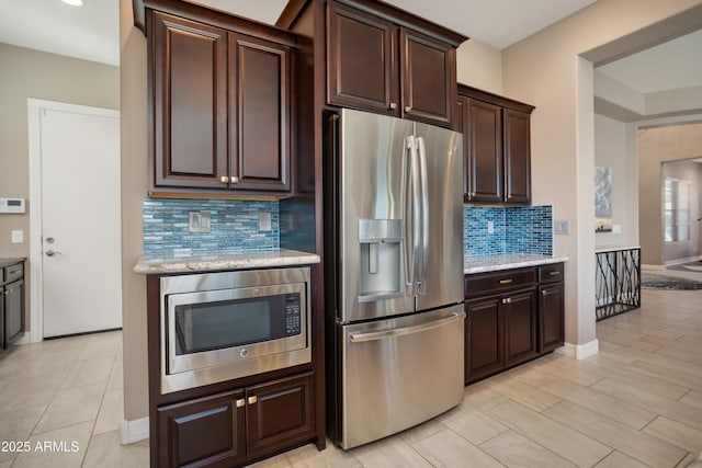 kitchen featuring light stone counters, appliances with stainless steel finishes, baseboards, dark brown cabinetry, and backsplash