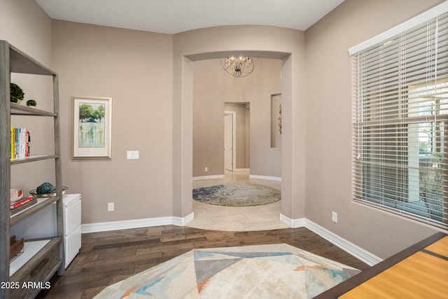 corridor featuring wood finished floors, a chandelier, and baseboards
