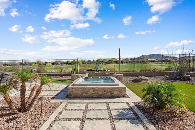 view of patio featuring a mountain view, a fenced backyard, and an in ground hot tub