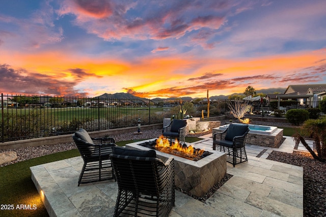 patio terrace at dusk with an outdoor fire pit, a mountain view, and a fenced backyard