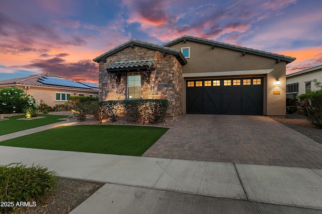 view of front facade with a front lawn, a garage, decorative driveway, stone siding, and stucco siding