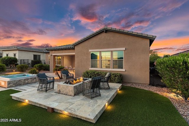 back of house at dusk with an outdoor fire pit, stucco siding, a tiled roof, an in ground hot tub, and a patio area