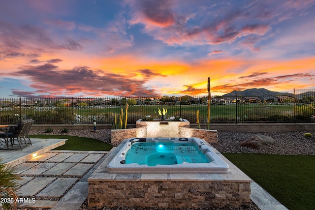 pool at dusk featuring a fenced backyard, an outdoor hot tub, a patio area, a mountain view, and a lawn