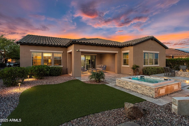 back of property with a patio, an in ground hot tub, a tile roof, stucco siding, and a yard