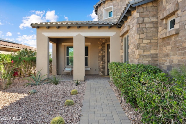 property entrance featuring a porch, stucco siding, and stone siding