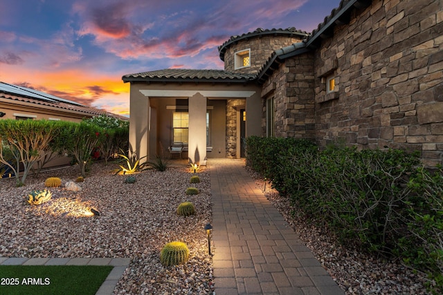 doorway to property featuring a porch, stucco siding, a tiled roof, and stone siding