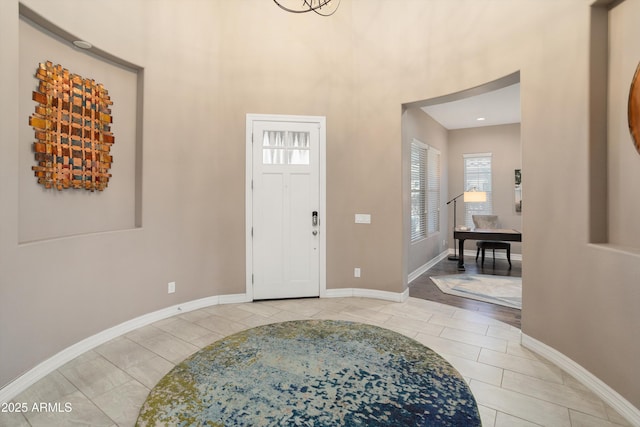 entrance foyer with light tile patterned floors, a towering ceiling, and baseboards