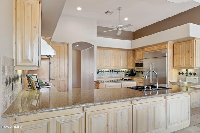 kitchen with built in appliances, light brown cabinetry, arched walkways, and visible vents