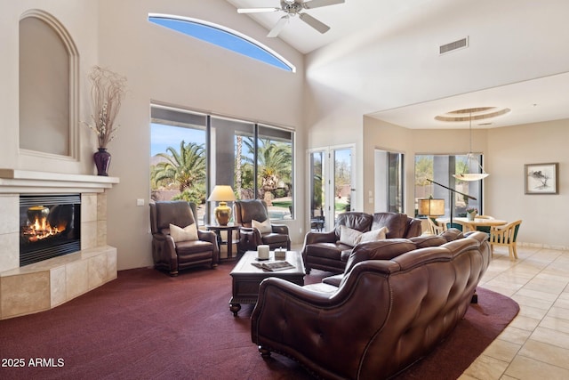 tiled living room featuring carpet, a fireplace, visible vents, a towering ceiling, and a ceiling fan