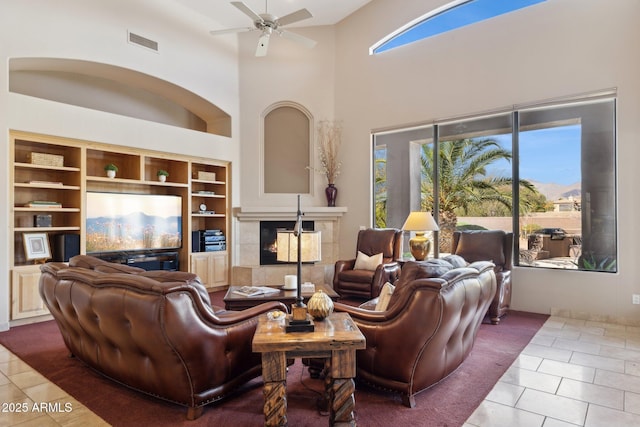 tiled living area with ceiling fan, a high ceiling, visible vents, and a tiled fireplace