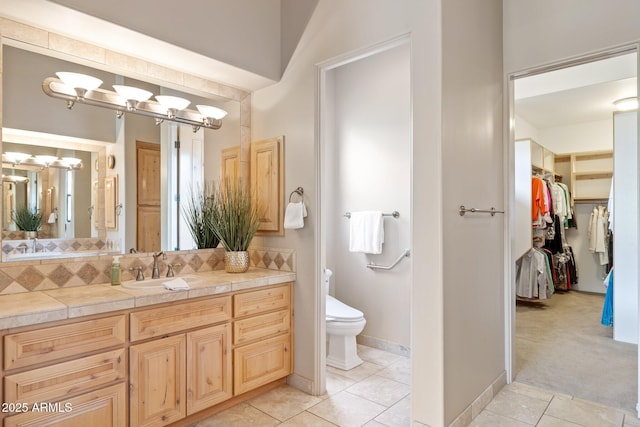 full bath with toilet, tile patterned flooring, a spacious closet, vanity, and backsplash