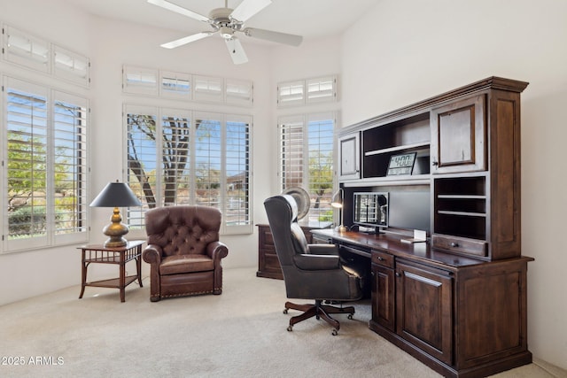 home office with ceiling fan, a towering ceiling, and light colored carpet