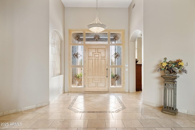 foyer entrance featuring a towering ceiling, baseboards, and arched walkways