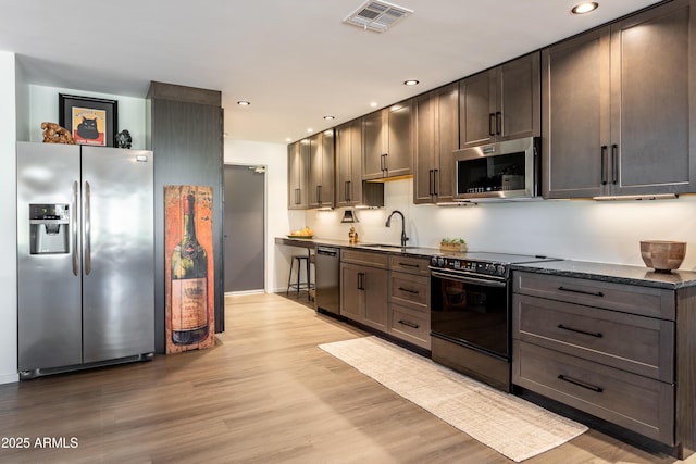 kitchen with black appliances, sink, dark stone counters, dark brown cabinetry, and light hardwood / wood-style floors