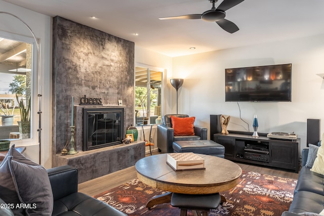 living room featuring wood-type flooring, a large fireplace, and ceiling fan