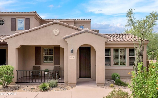 mediterranean / spanish-style house featuring covered porch, a tiled roof, and stucco siding