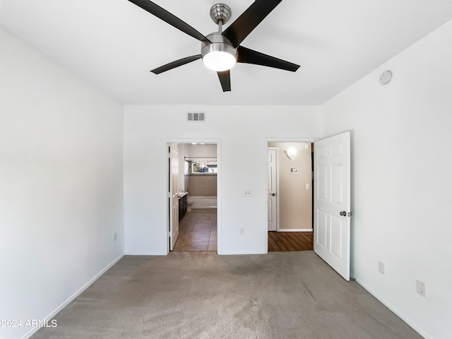 unfurnished bedroom featuring ceiling fan, light colored carpet, and ensuite bath