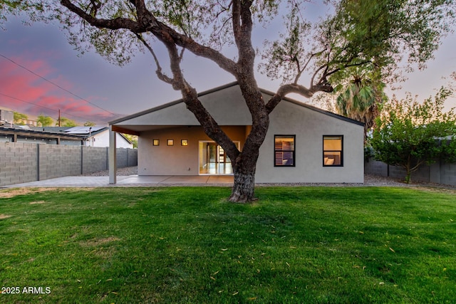 back of property at dusk featuring a lawn, a patio, a fenced backyard, and stucco siding