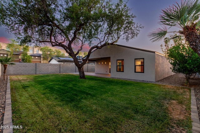 back of house at dusk featuring fence, stucco siding, and a yard