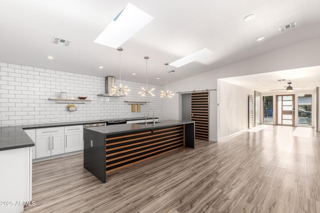 kitchen featuring visible vents, dark countertops, a barn door, wall chimney exhaust hood, and a sink
