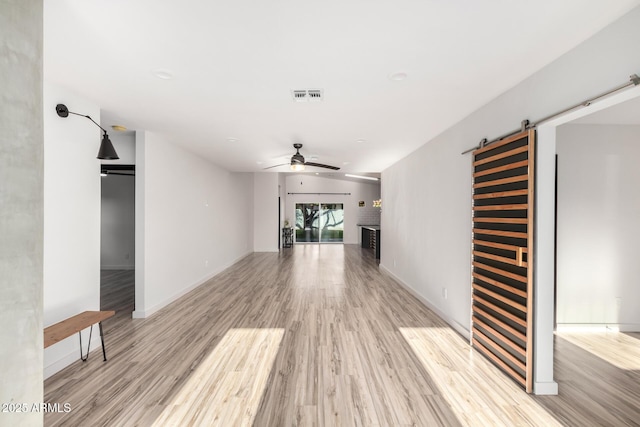 unfurnished living room with visible vents, a fireplace, ceiling fan, a barn door, and light wood-style flooring