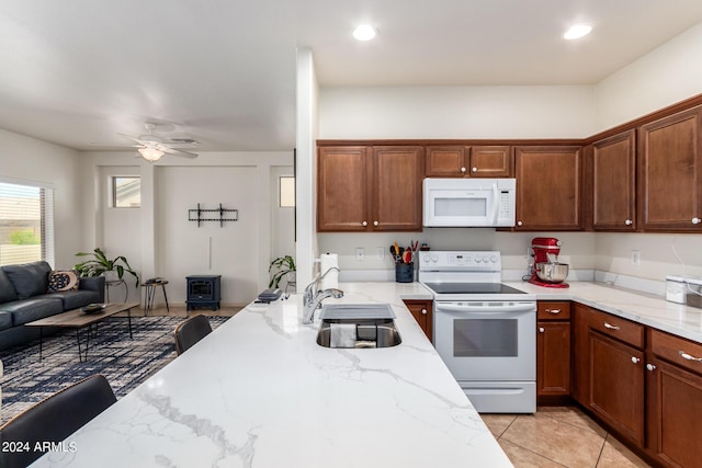 kitchen featuring sink, white appliances, light stone counters, light tile patterned floors, and a breakfast bar area