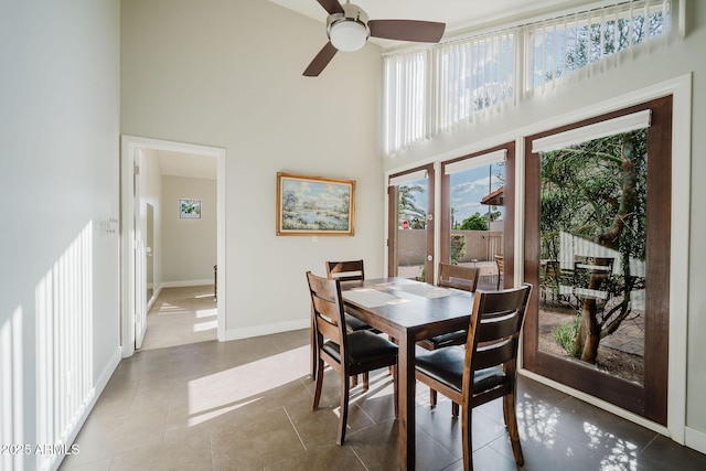 tiled dining room featuring a towering ceiling, ceiling fan, and baseboards