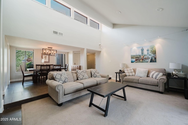 living area with baseboards, visible vents, an inviting chandelier, and a towering ceiling