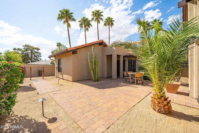 rear view of property featuring a tile roof, fence, stucco siding, and a patio area