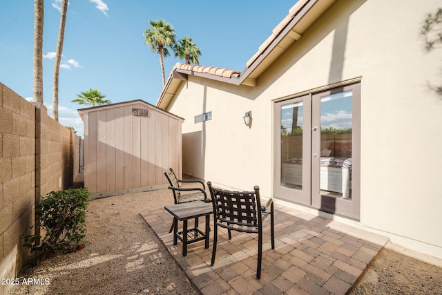 view of patio / terrace with outdoor dining area, an outdoor structure, a storage unit, french doors, and fence