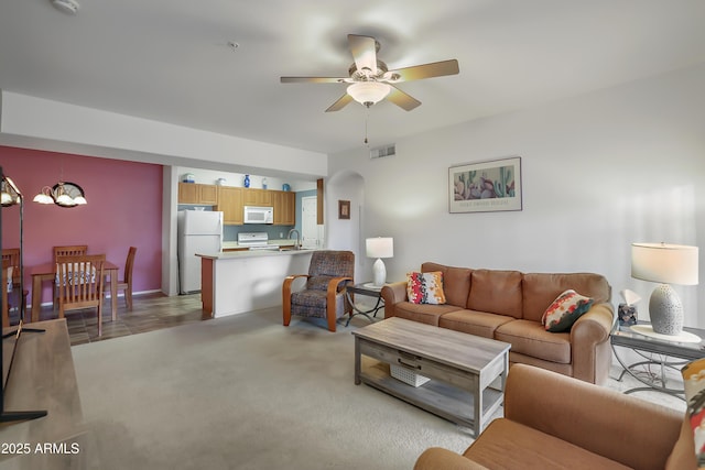 carpeted living room with ceiling fan with notable chandelier and sink