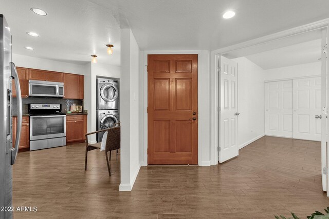 kitchen with stainless steel appliances, stacked washing maching and dryer, backsplash, and dark wood-type flooring