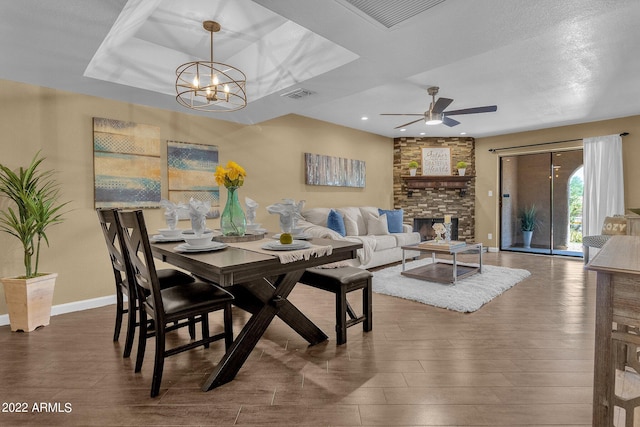 dining area with a textured ceiling, a fireplace, ceiling fan with notable chandelier, a tray ceiling, and dark hardwood / wood-style floors