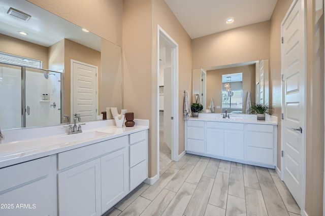 bathroom with a shower stall, two vanities, visible vents, and a sink