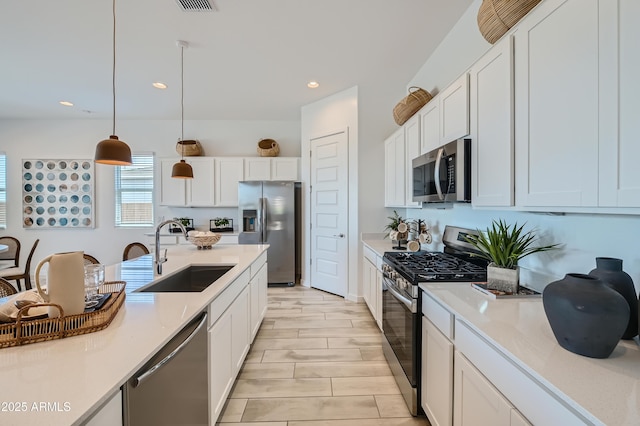 kitchen with a sink, decorative light fixtures, appliances with stainless steel finishes, white cabinets, and light countertops