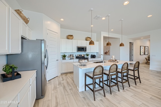 kitchen with a breakfast bar, light wood-style flooring, appliances with stainless steel finishes, white cabinets, and a sink