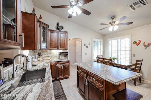 kitchen featuring lofted ceiling, backsplash, sink, dark brown cabinets, and a kitchen island