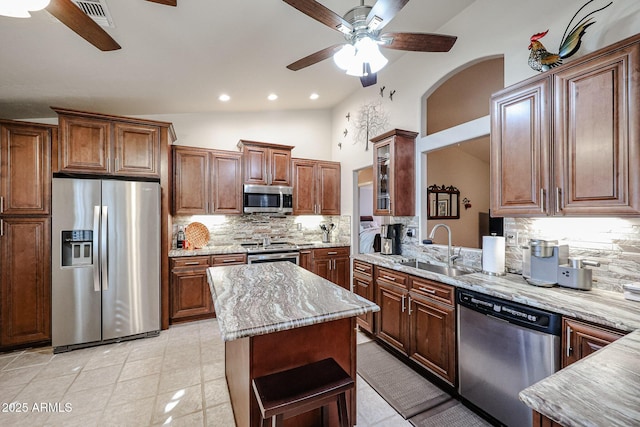 kitchen with sink, stainless steel appliances, tasteful backsplash, light stone counters, and lofted ceiling