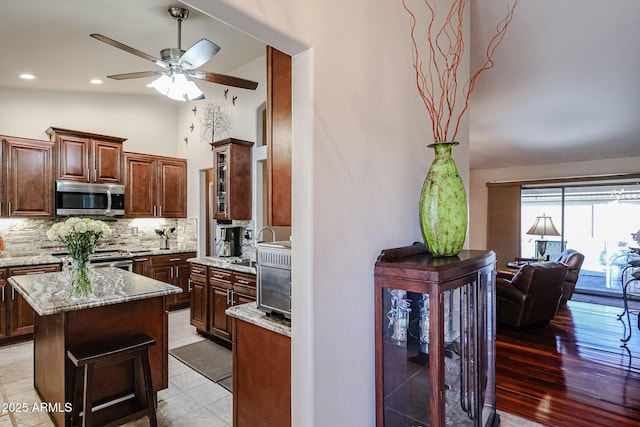 kitchen with ceiling fan, tasteful backsplash, lofted ceiling, a kitchen island, and appliances with stainless steel finishes