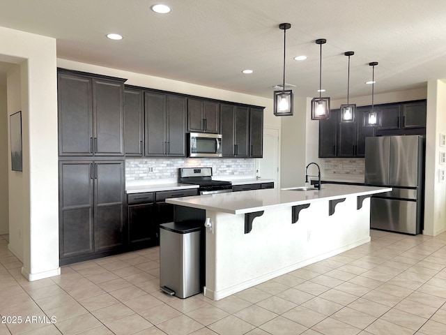 kitchen with a breakfast bar area, decorative light fixtures, light tile patterned floors, appliances with stainless steel finishes, and an island with sink