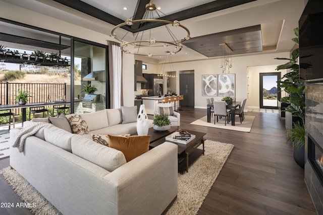 living room with an inviting chandelier, dark wood-type flooring, a tray ceiling, and a tiled fireplace