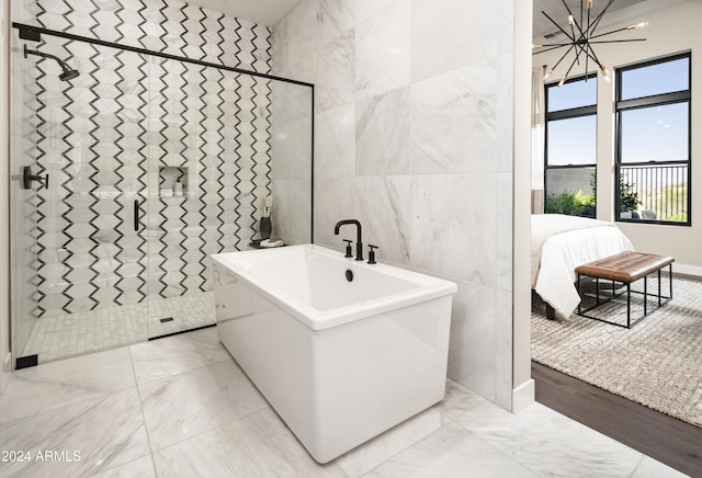 bathroom with tile walls, shower with separate bathtub, and a notable chandelier