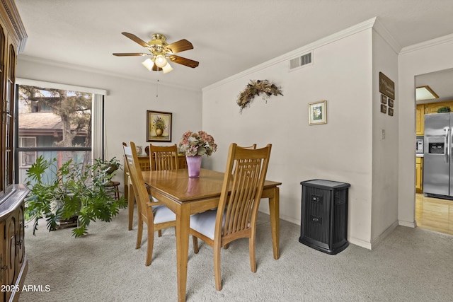 dining space with baseboards, visible vents, light colored carpet, ceiling fan, and ornamental molding