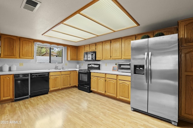 kitchen featuring a toaster, light countertops, visible vents, light wood-type flooring, and black appliances