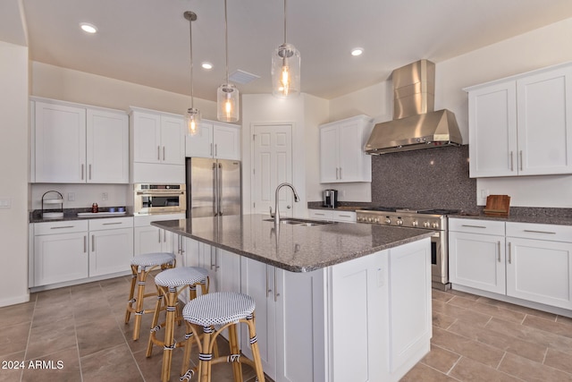 kitchen featuring high quality appliances, a center island with sink, sink, wall chimney exhaust hood, and decorative light fixtures