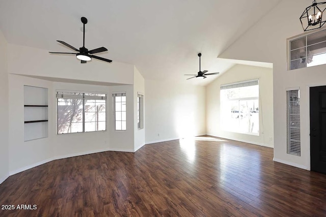 unfurnished living room featuring lofted ceiling, dark hardwood / wood-style floors, a wealth of natural light, and ceiling fan with notable chandelier