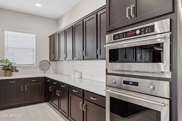 kitchen featuring decorative backsplash, dark brown cabinetry, double oven, and light countertops