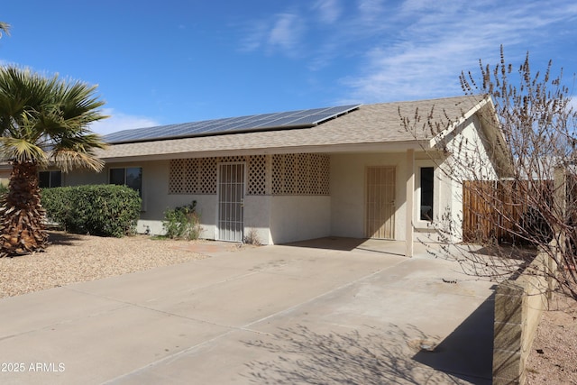 ranch-style house featuring solar panels, roof with shingles, driveway, and stucco siding