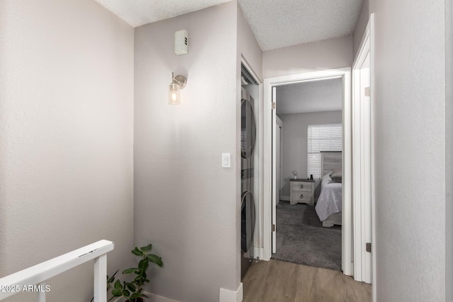 hallway with a textured ceiling, light hardwood / wood-style floors, and stacked washer and clothes dryer